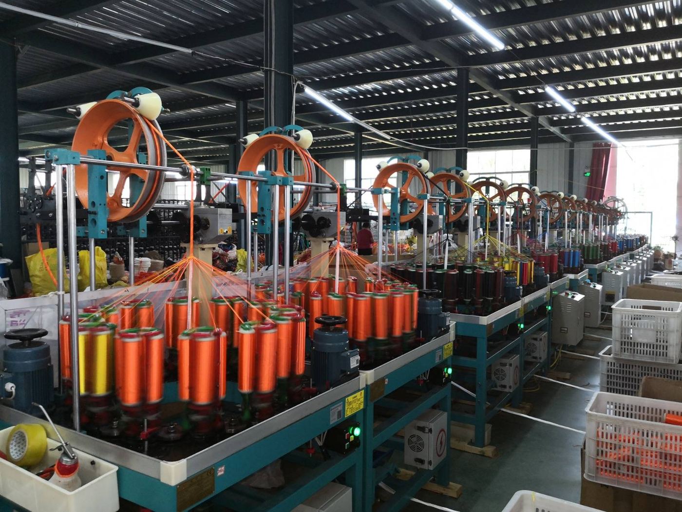 Rows of braiding machines running orange yarn in the Orange Vision workshop